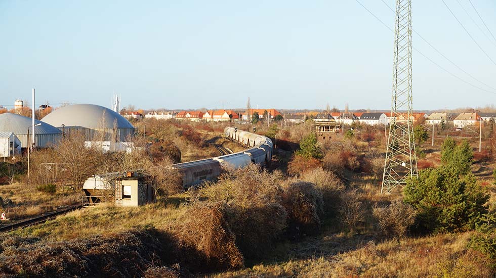 Ausblick auf eine Landschaft aus Industriegebäuden, kleinen Baumgruppen und Wohngebäuden von einer Brücke in der Nähe des Bahnhofs Bitterfeld.